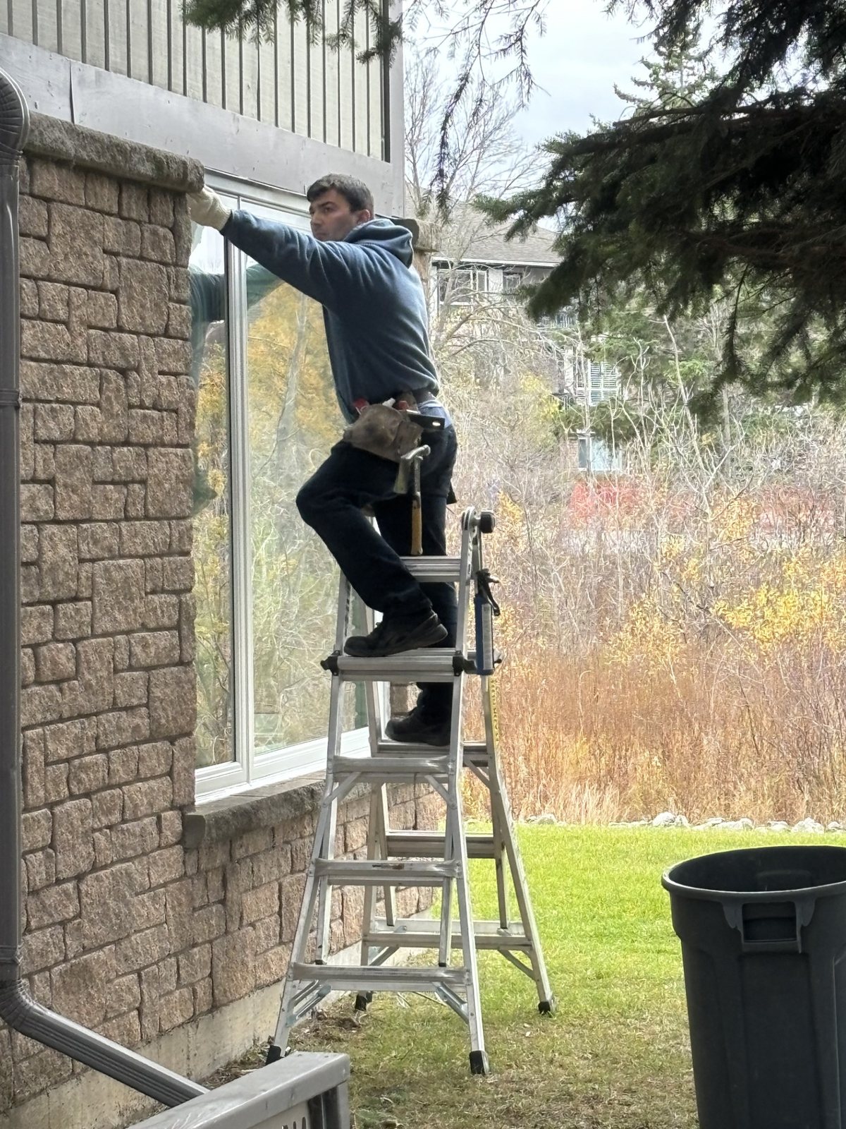 Real WDC installer on a ladder setting a window on a brick home